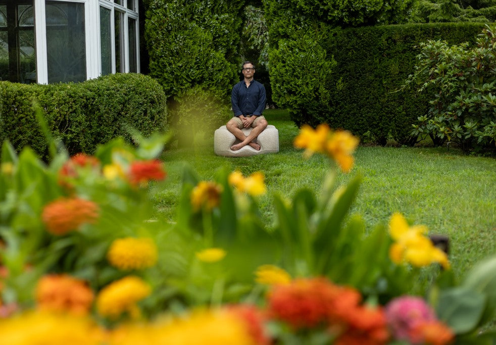 A person sitting cross-legged on an Oyster Meditation Chair in a garden