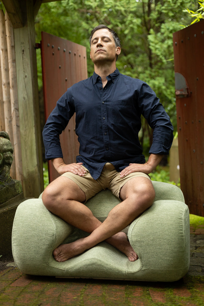 A person sitting cross-legged on a green Oyster Meditation Chair